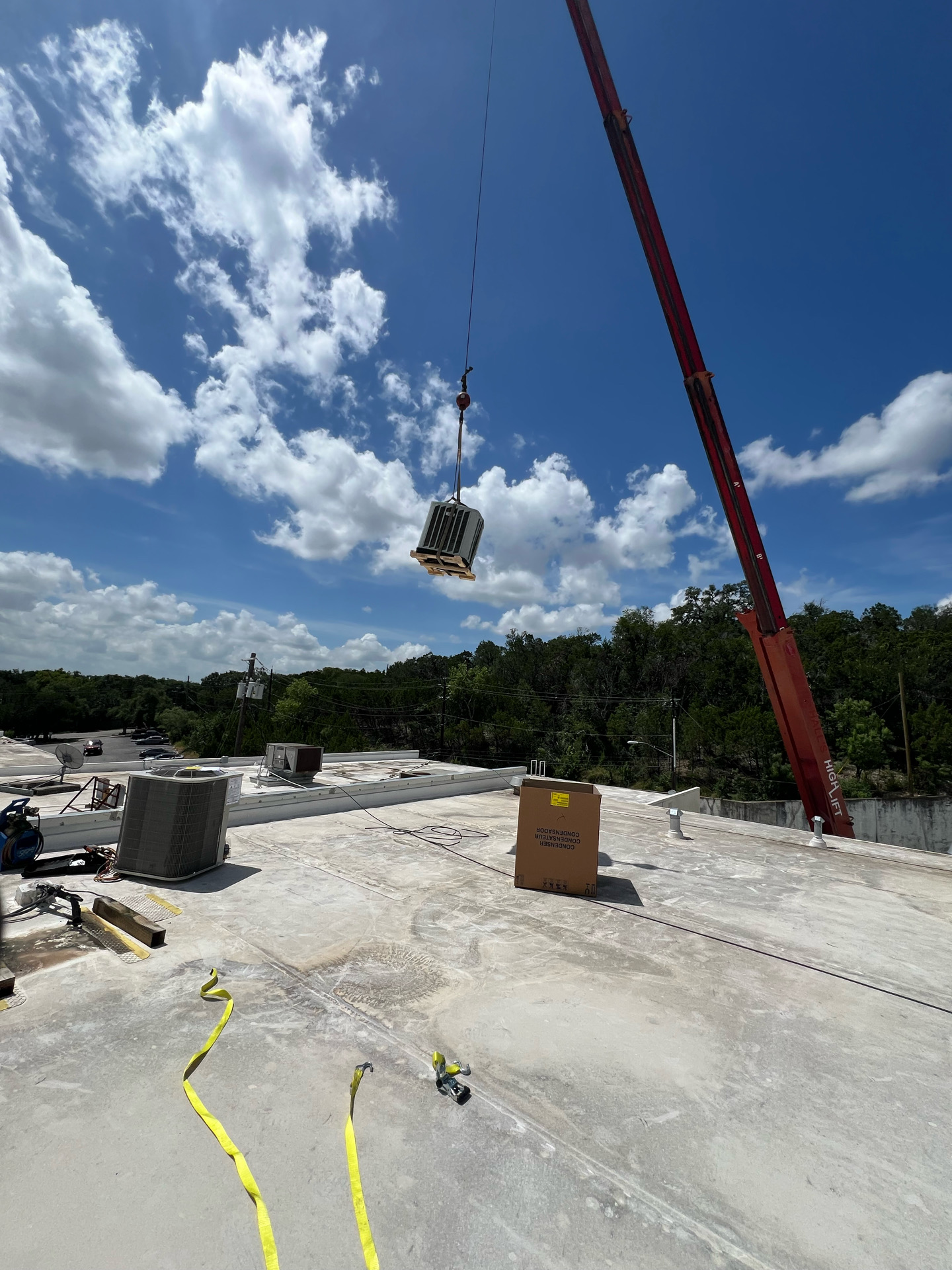 Crane lifting an HVAC unit above a commercial rooftop